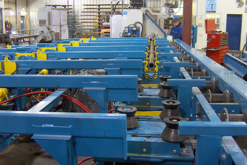 Powered feed conveyor to a CNC turning center. Feed features V pinch rollers and steady rests to support the pipe while being threaded.